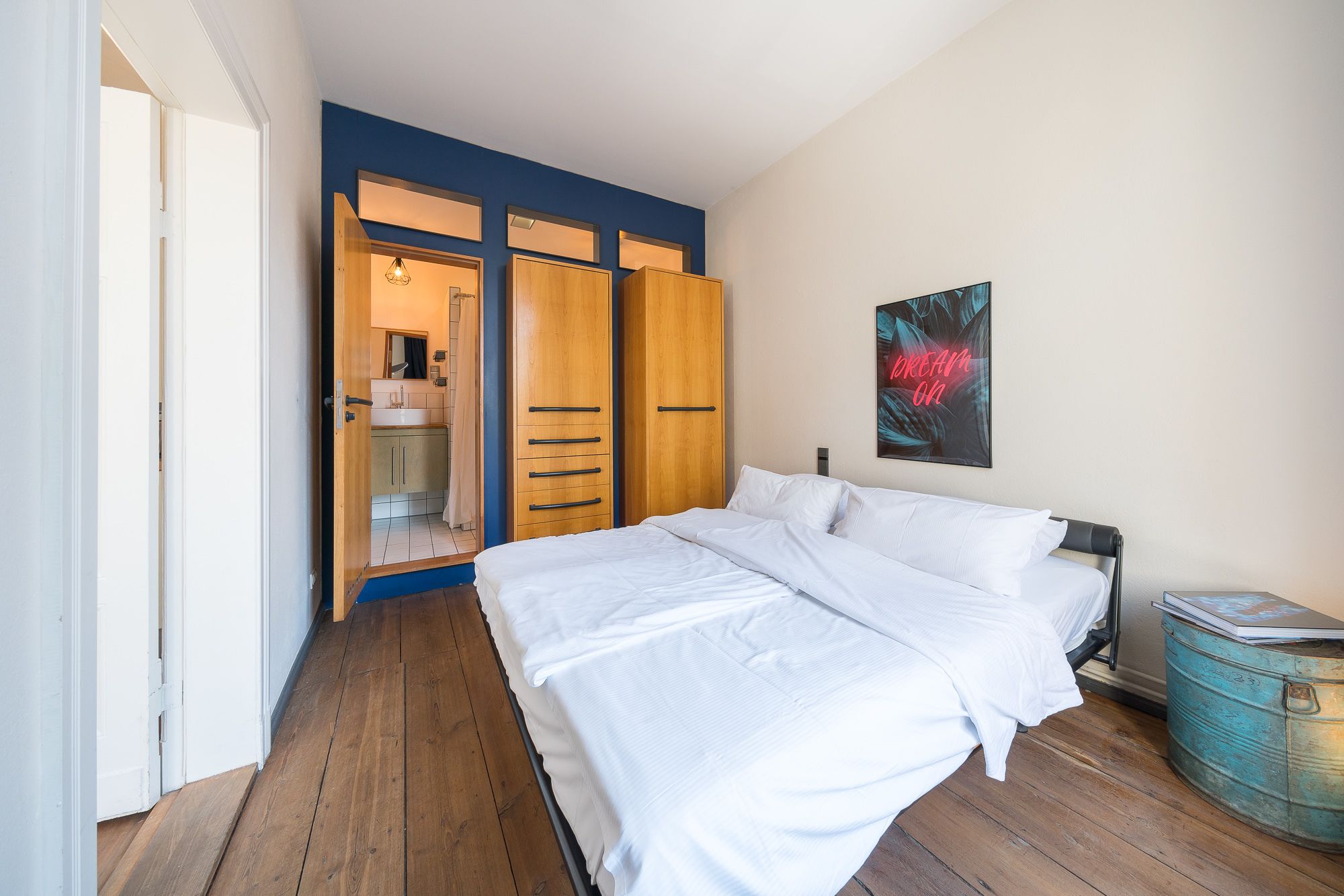 A bedroom with a wooden wardrobe, a bed with white linens, and a blue wall.