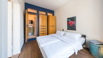 A bedroom with a wooden wardrobe, a bed with white linens, and a blue wall.