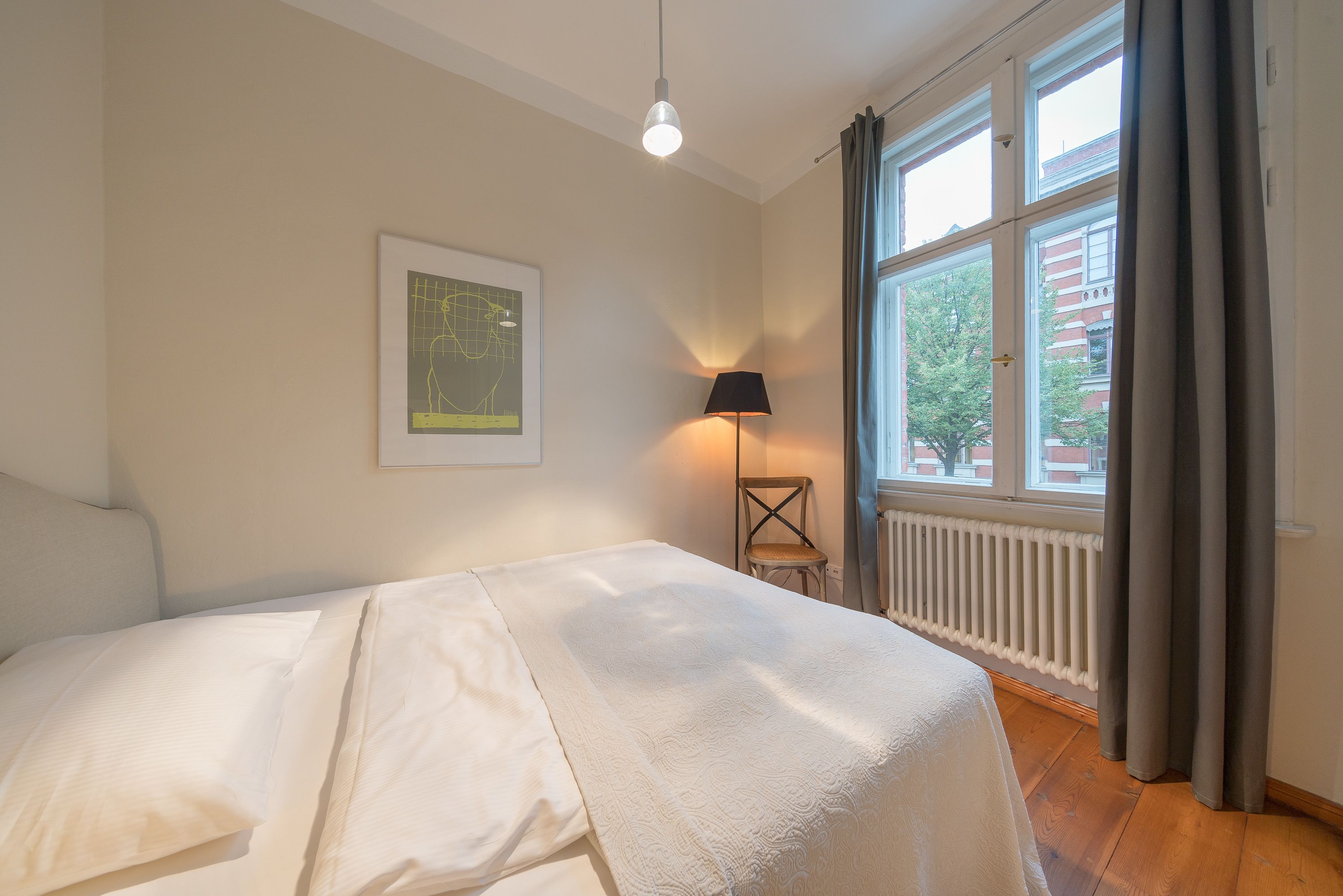 Un dormitorio con cama, lámpara, radiador y ventana con cortinas.