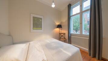 Un dormitorio con cama, lámpara, radiador y ventana con cortinas.