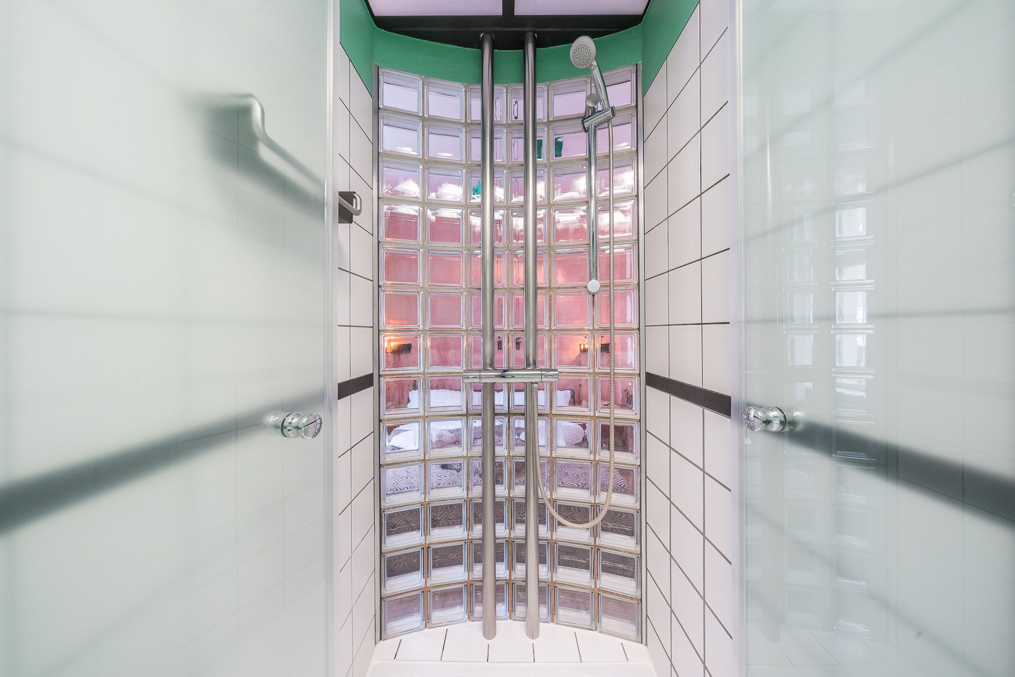 Un baño moderno con cabina de ducha de vidrio, azulejos blancos y una pared de acento verde.