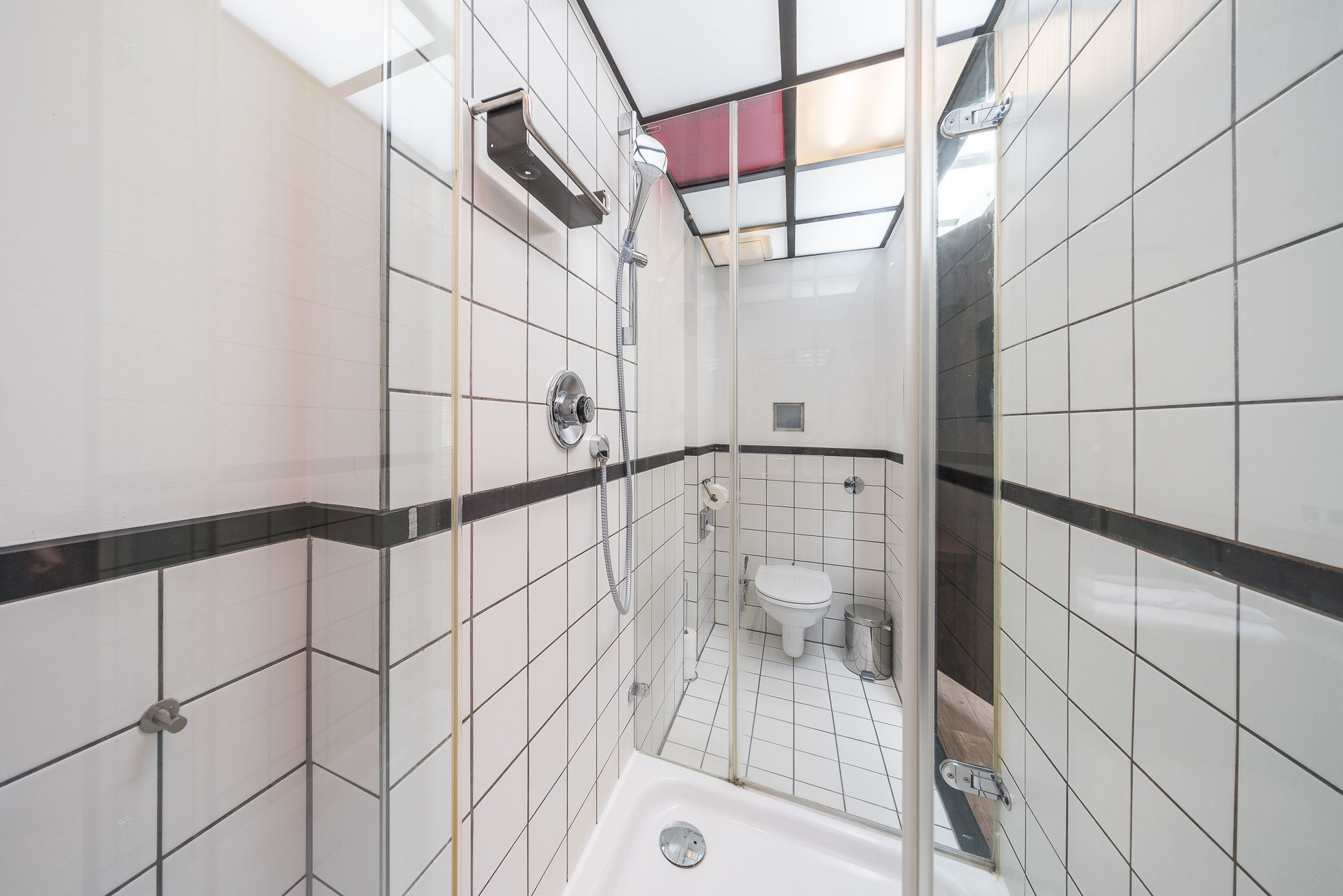 A small, tiled bathroom with a shower, toilet, and a glass partition.