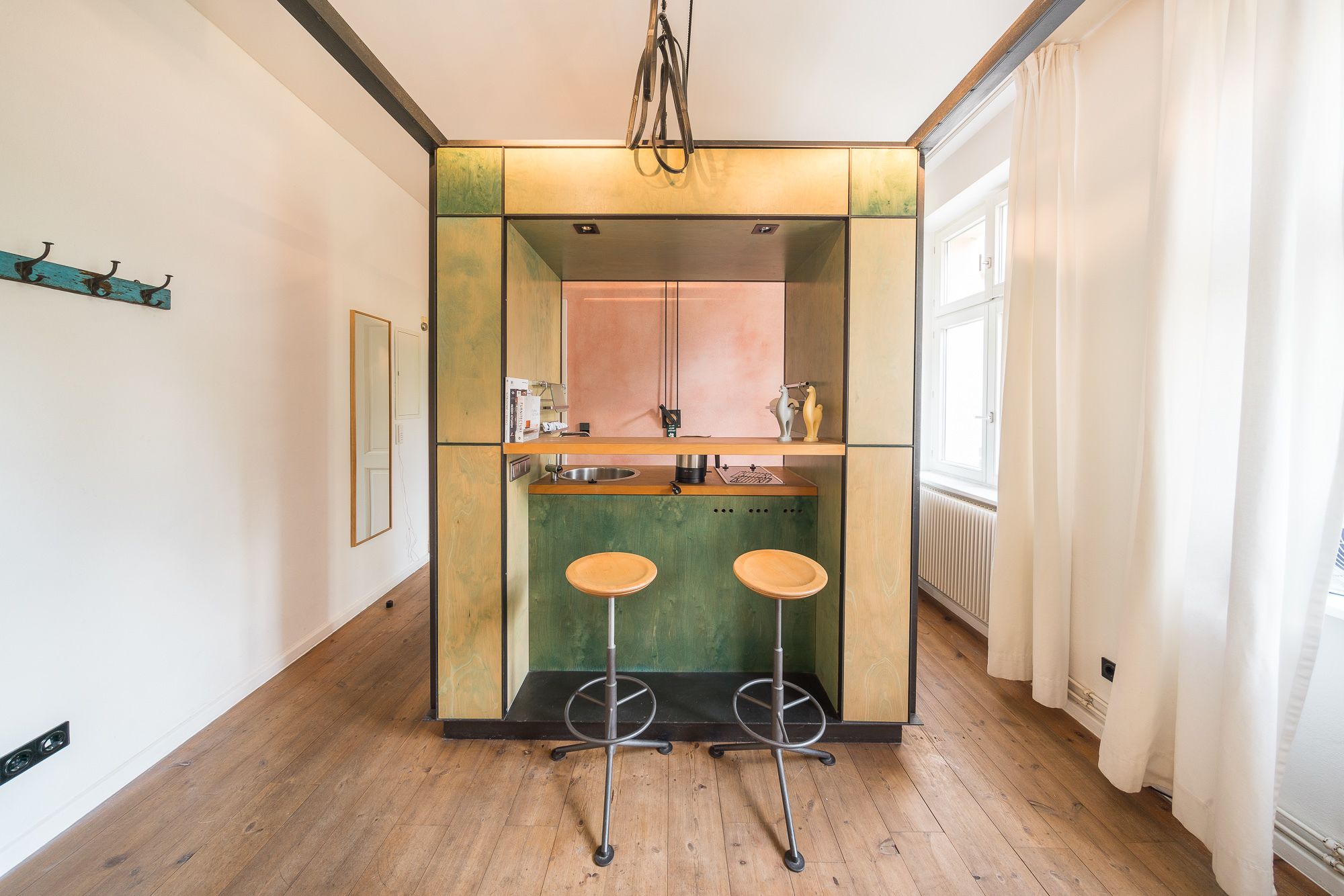 A compact kitchen with a central island, two stools, and a window with curtains.