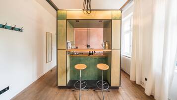 A compact kitchen with a central island, two stools, and a window with curtains.
