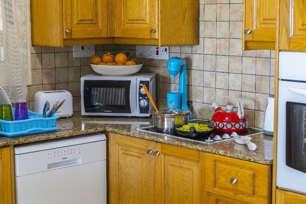 Une cuisine avec des meubles en bois, un four à micro-ondes, un grille-pain, une bouilloire et un saladier rempli d’oranges sur le plan de travail.