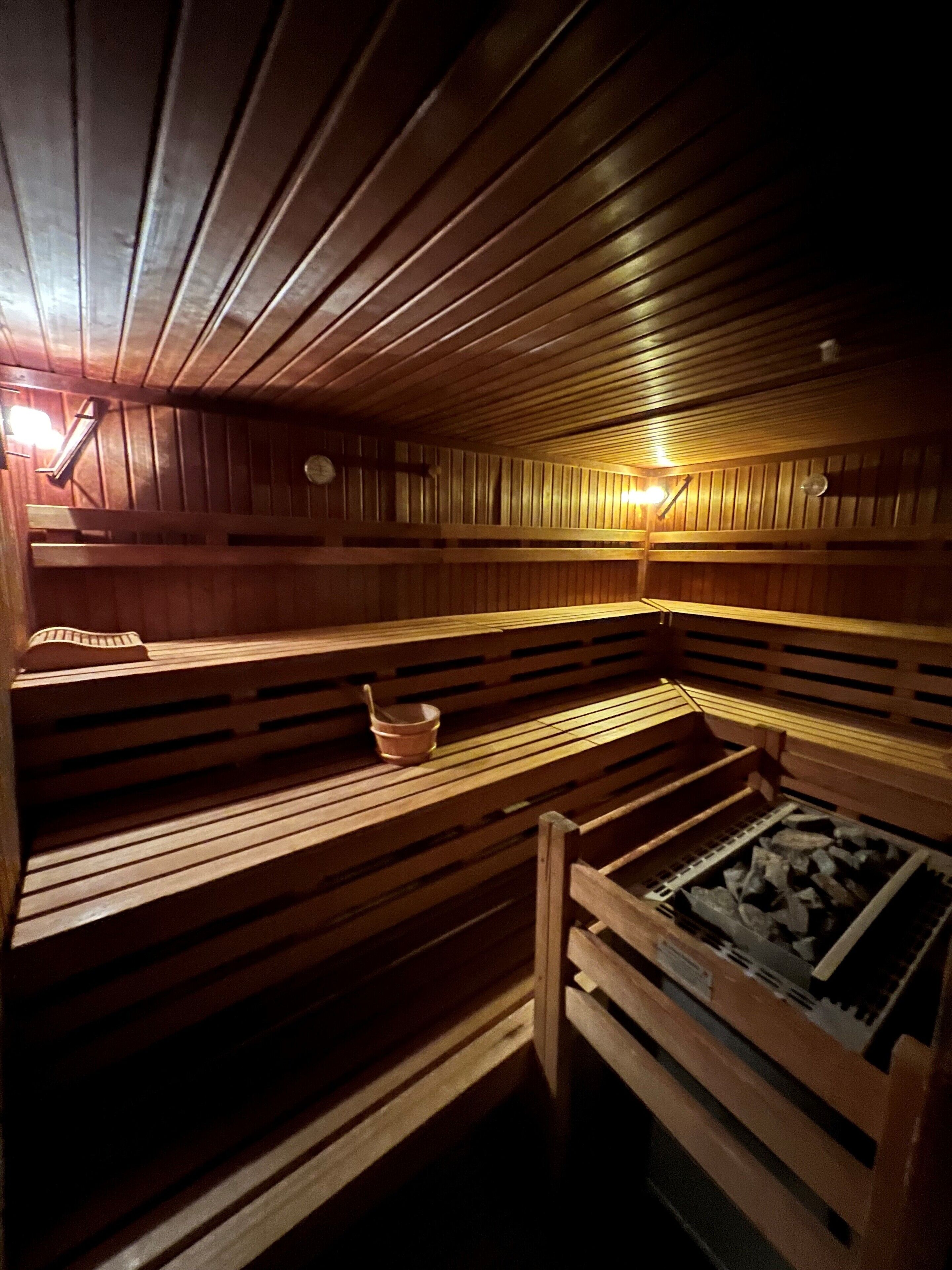 Una sauna con bancos de madera, una mesa pequeña con un tazón y un calentador.