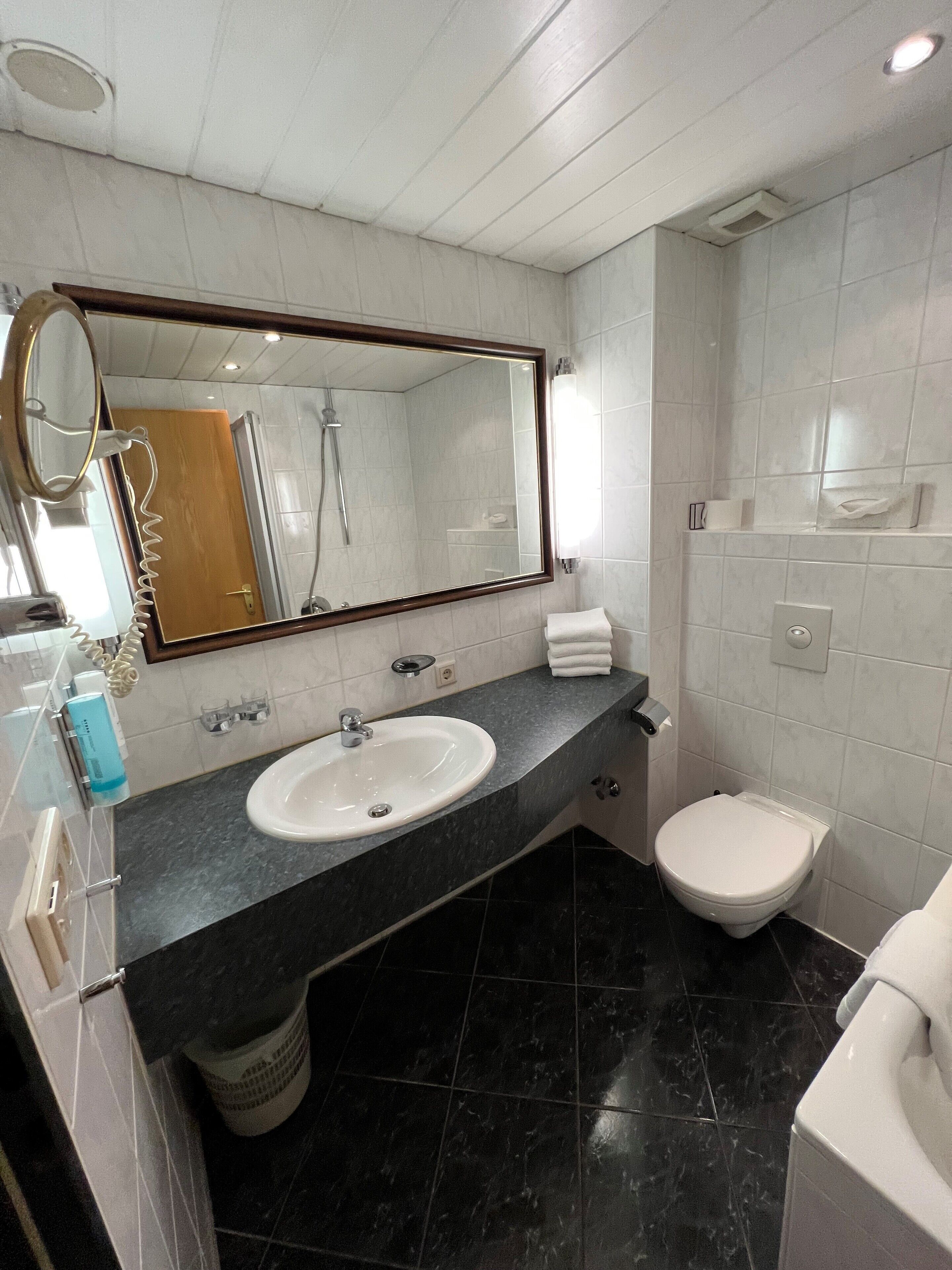 Un baño moderno con un espejo grande, un lavamanos, un inodoro y una ducha.