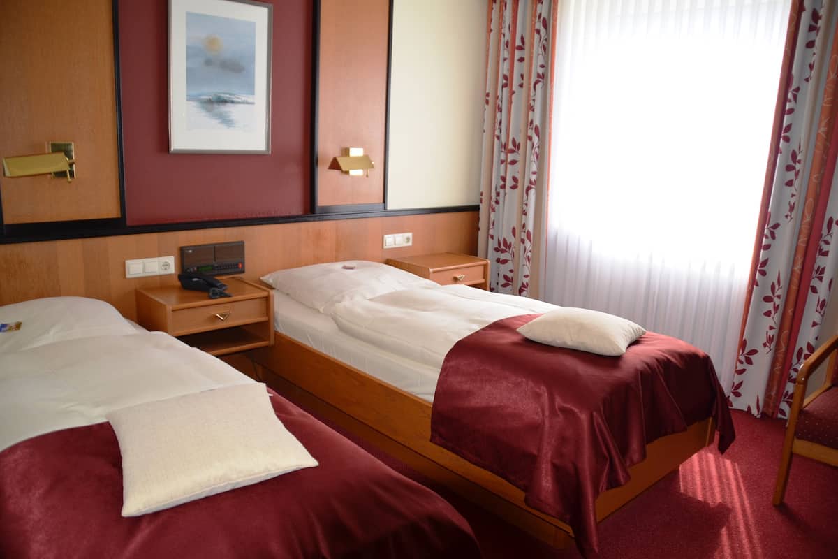 A hotel room with two beds, a wooden nightstand, a desk, and a chair.