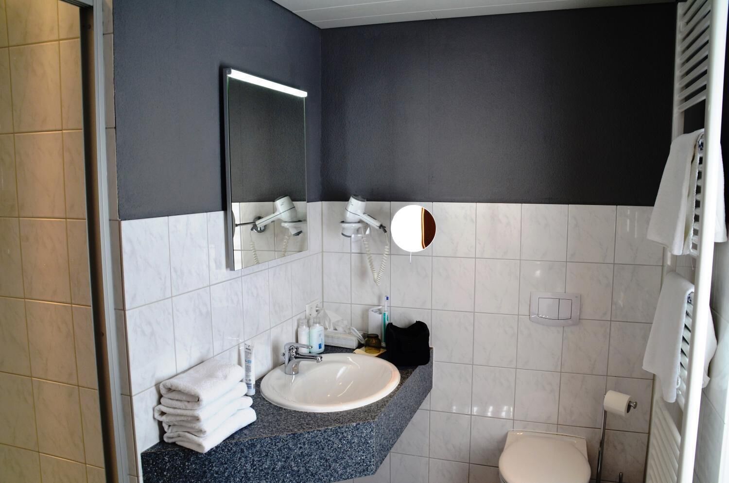 Ein modernes Badezimmer mit einem weißen Waschbecken, einer dunklen Wand und einem Spiegel darüber.