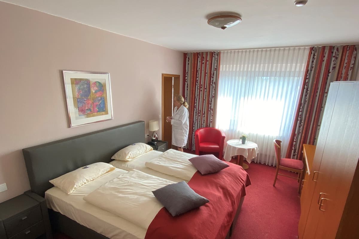 A hotel room with a large bed, a bedside table, a chair, a small table with a plant, and a wardrobe.