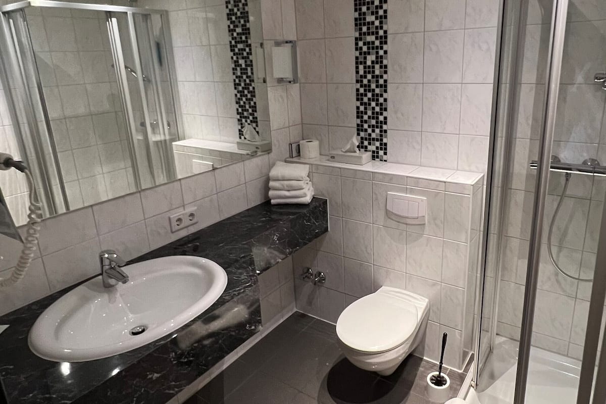 A modern bathroom with a marble sink, a toilet, and a glass shower enclosure.