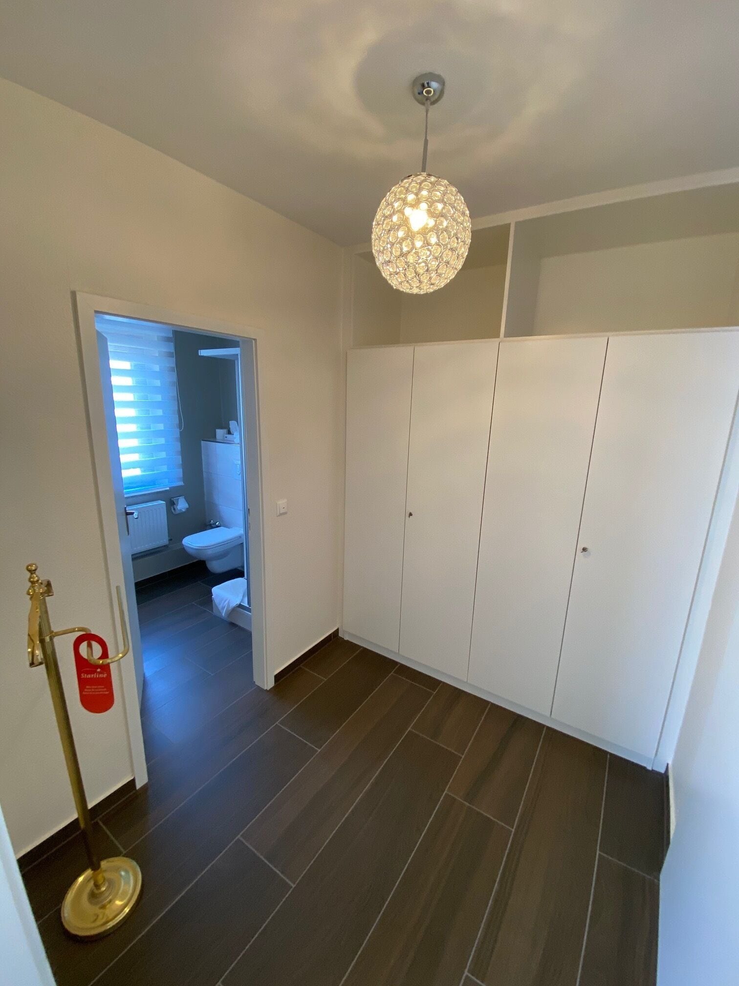 Una habitación con armario, lámpara de pie y baño visible a través de una puerta abierta.