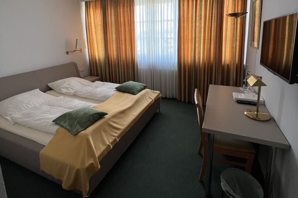 A hotel room with two beds, a desk, a chair, a lamp, and a trash bin.