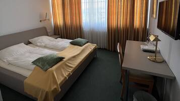 Una habitación de hotel con dos camas, un escritorio, una silla, una lámpara y un cubo de basura.