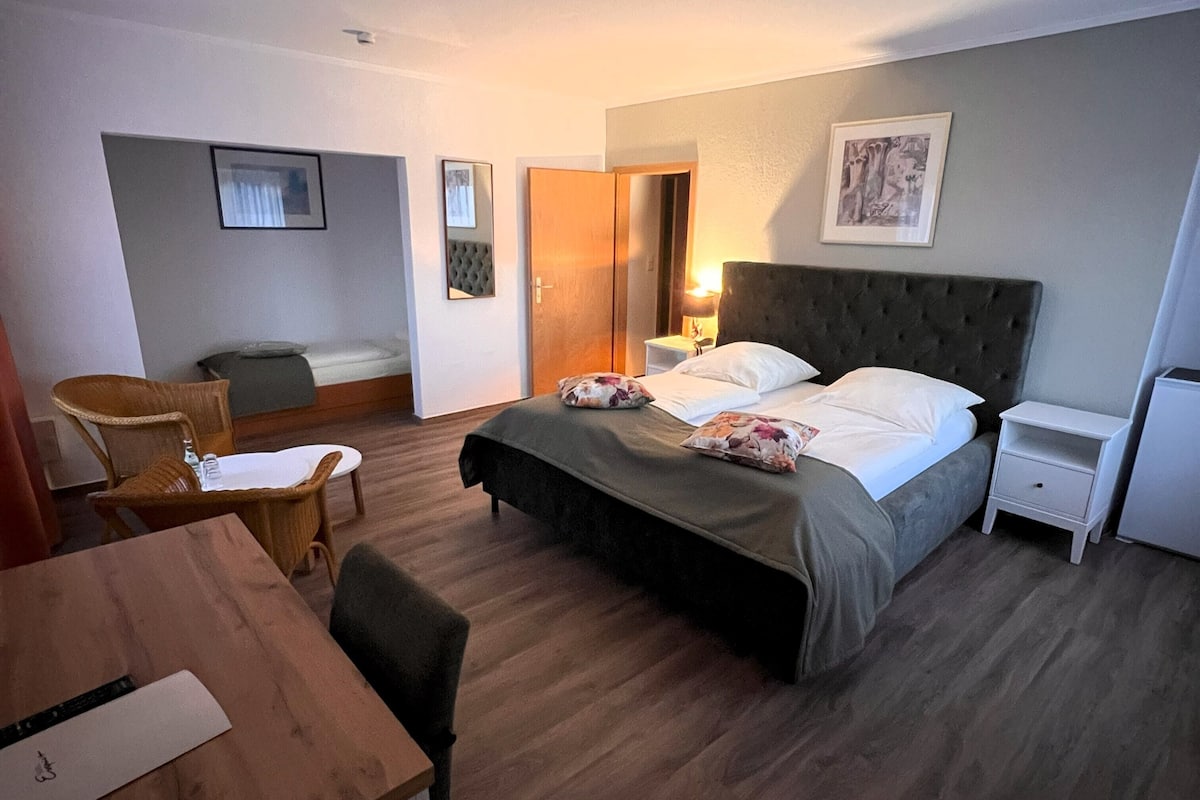 A hotel room with a bed, a desk, a chair, a nightstand, and a bedside table.