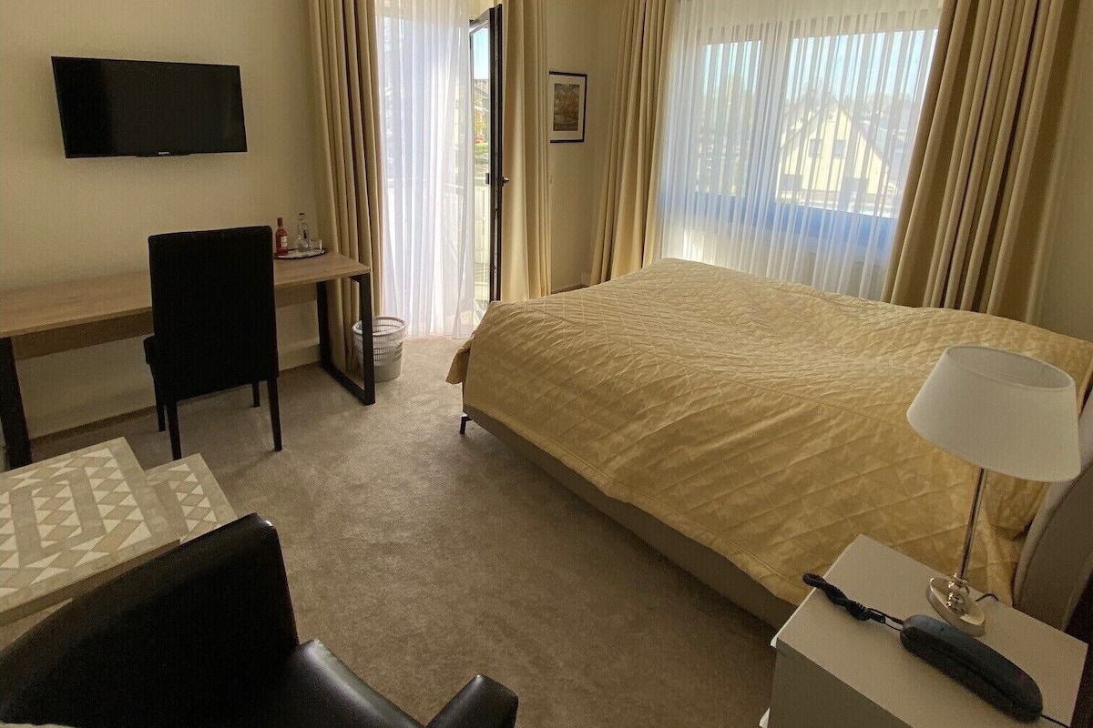 A hotel room with a bed, a desk, a chair, a TV, and a lamp.