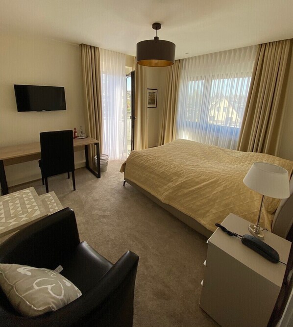 A hotel room with a bed, a desk, a chair, a TV, and a lamp.