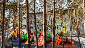 A playground with various play structures surrounded by trees and a stone building in the background.