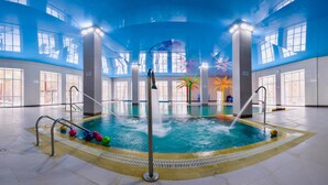 An indoor swimming pool with a central water feature, surrounded by windows and a high ceiling.