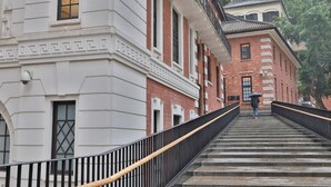 A staircase leading up to a building with a white facade and a red brick building in the background. - Butterfly on LKF, Central (Hong Kong)