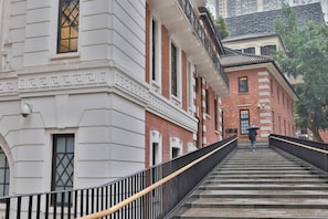 A staircase leading up to a building with a white facade and a red brick building in the background. - Butterfly on LKF, Central (Hong Kong)