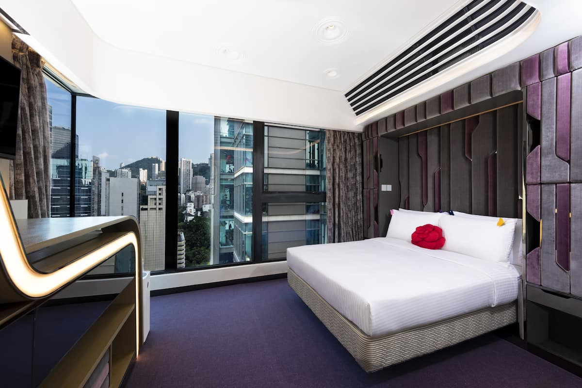 A modern hotel room with a large bed, a desk, and a city view.