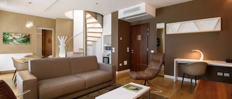 A modern living room with a sofa, armchairs, a coffee table, and a desk with a chair. There is a staircase leading to another level.