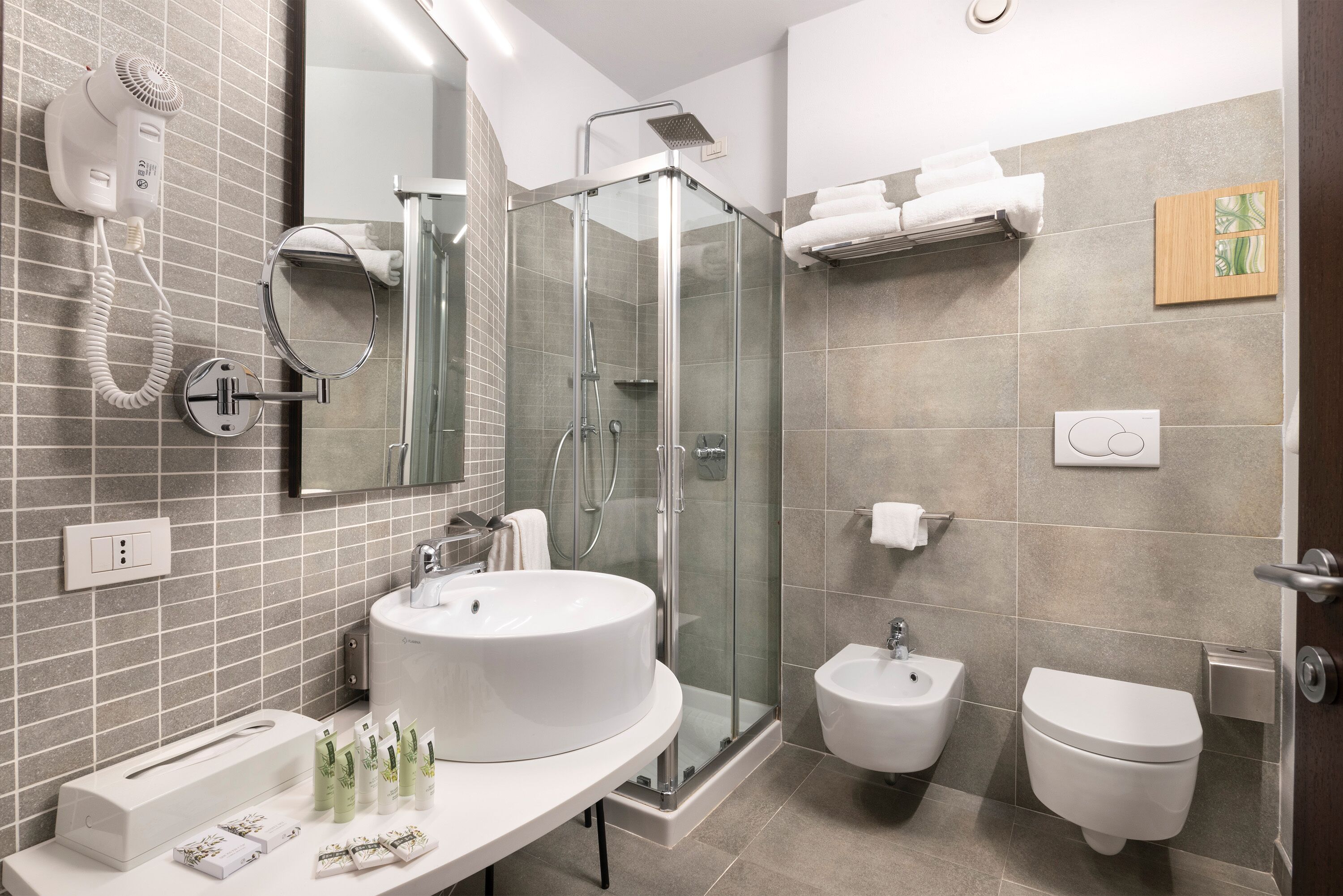 A modern bathroom with a glass-enclosed shower, a white sink, a bidet, and a toilet.