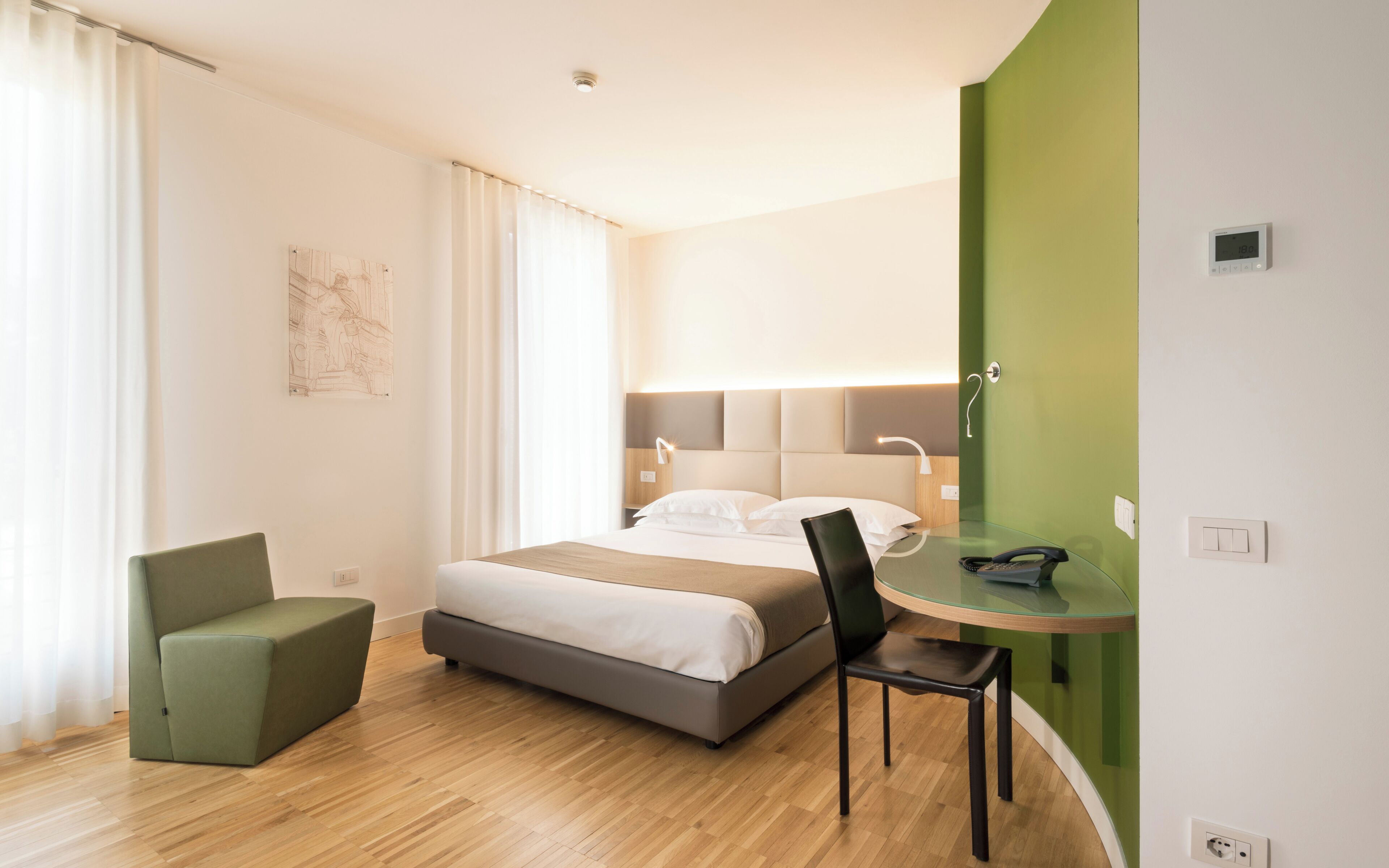Een hotelkamer met een bed, een bureau met stoel, een telefoon en een wandlamp.