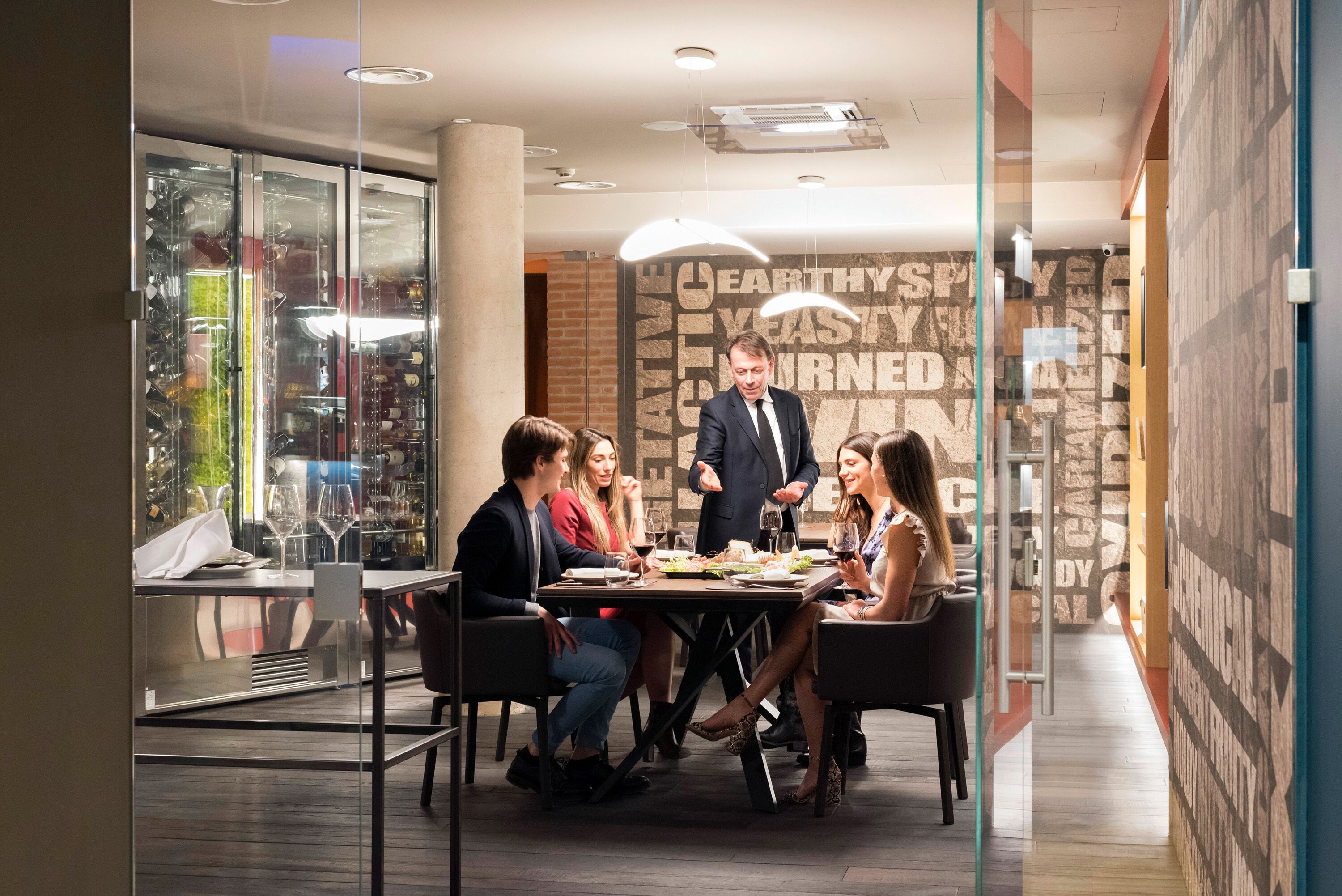 A modern conference room with a glass partition, a table with wine glasses, and a man presenting.