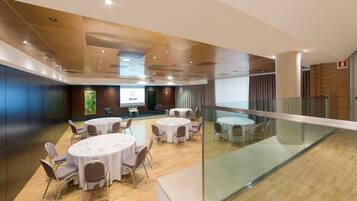 Una sala de conferencias moderna con mesas y sillas redondas, una pantalla de presentación y una barandilla de cristal con vistas a un nivel inferior.