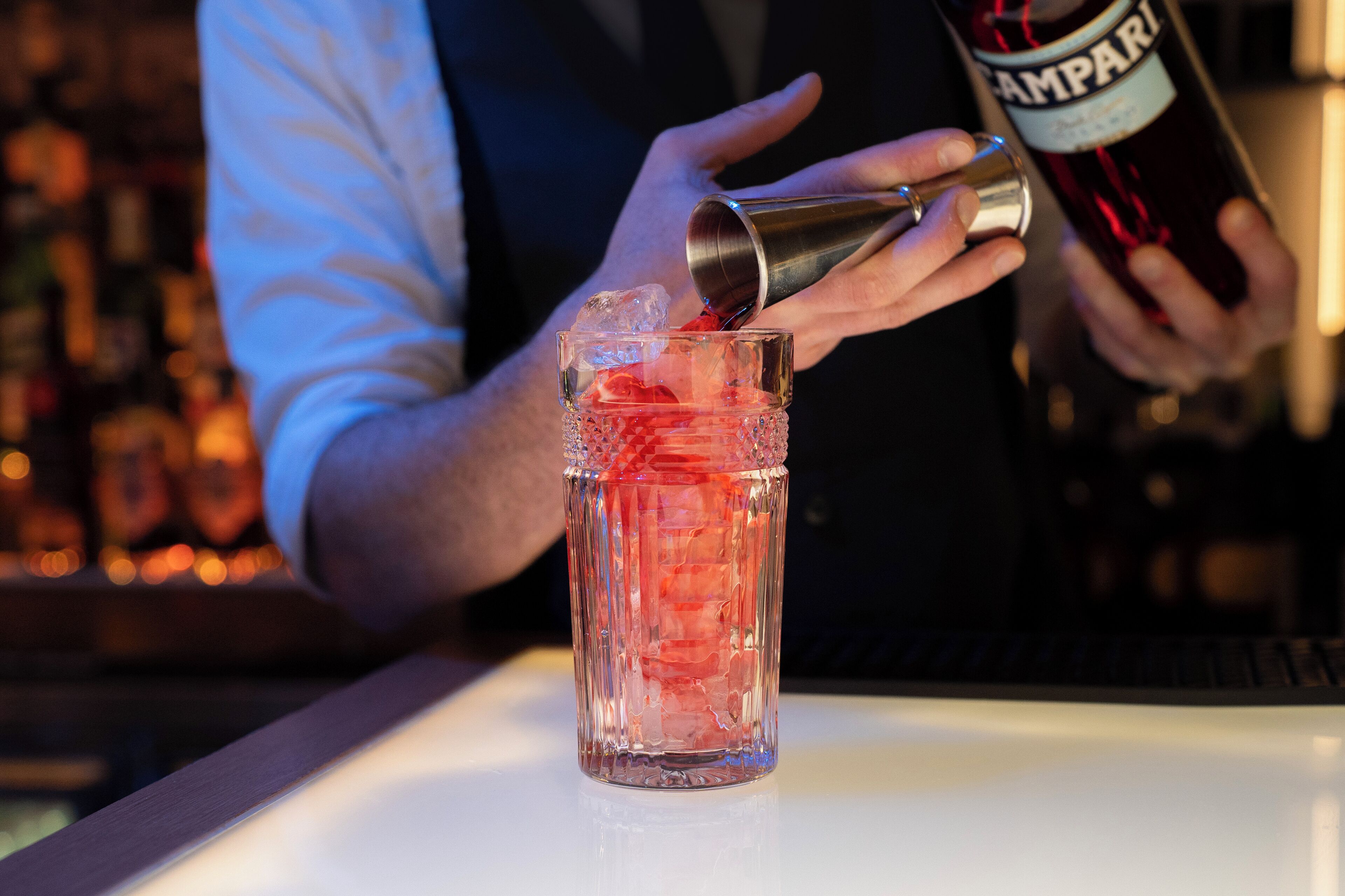 A bartender pouring a drink from a bottle into a glass.