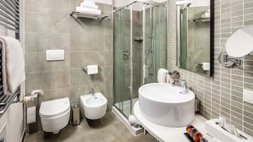 Ein modernes Badezimmer mit einer gläsernen Duschkabine, einem Bidet, einer Toilette und einem großen Waschbecken mit Spiegel.