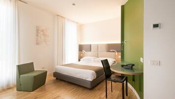 A modern hotel room with a bed, a green armchair, a small table with a chair, and a green accent wall.