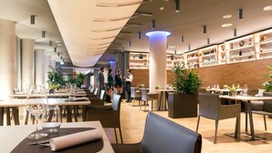 Een modern restaurant met een lange toonbank, meerdere tafels en een barruimte met flessenrekken.