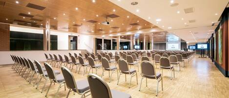 Un salón de conferencias con filas de sillas, suelo de madera y luces en el techo.