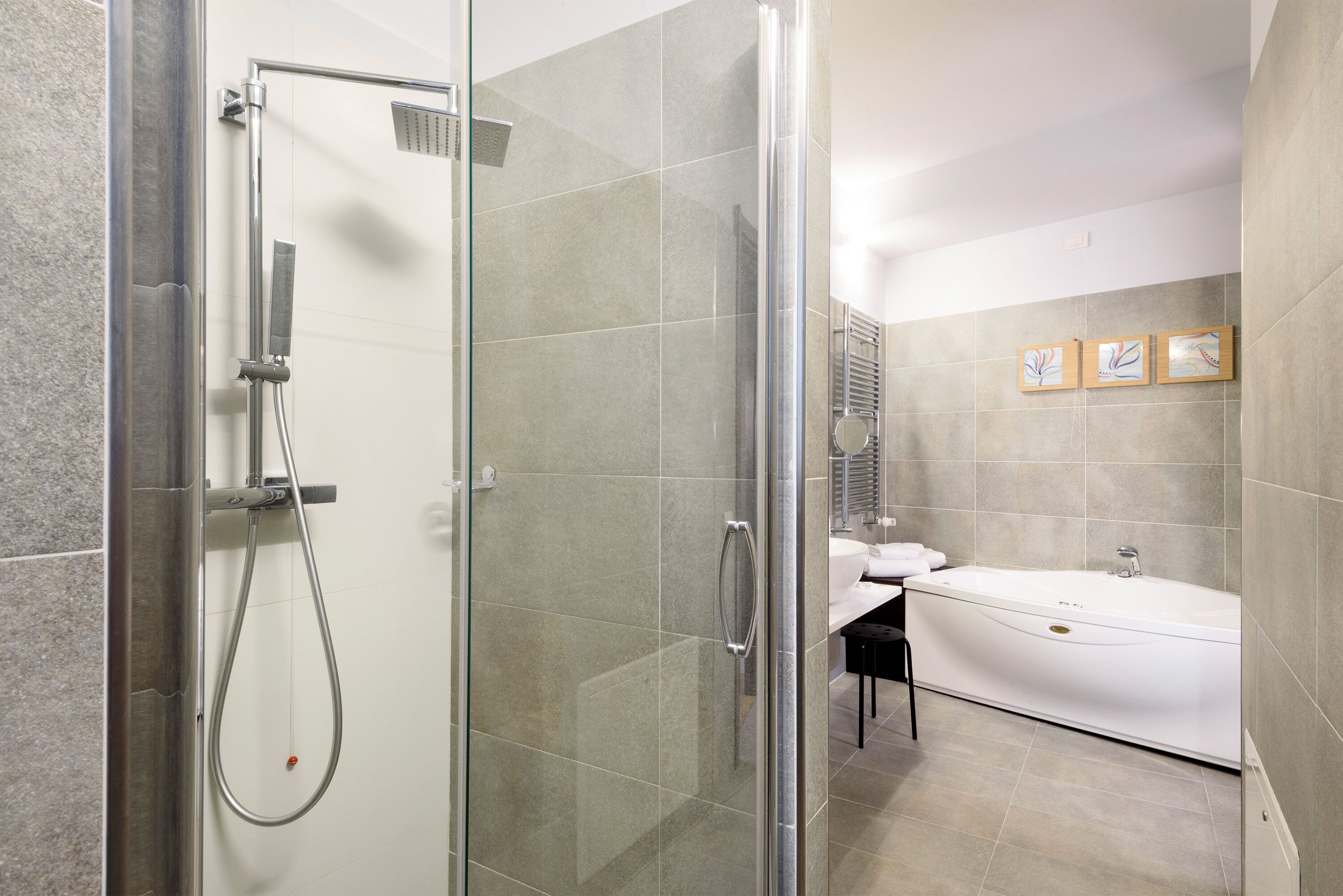 A modern bathroom with a glass-enclosed shower, a white bathtub, and a small stool.