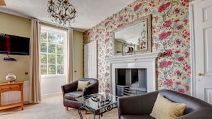 A living room with a fireplace, a television, and floral wallpaper. - White Linen Whitby, Room Only (Whitby)