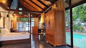Una habitación amplia con un gran armario de madera, una cama con sábanas blancas y vistas a una piscina por medio de una puerta de cristal.