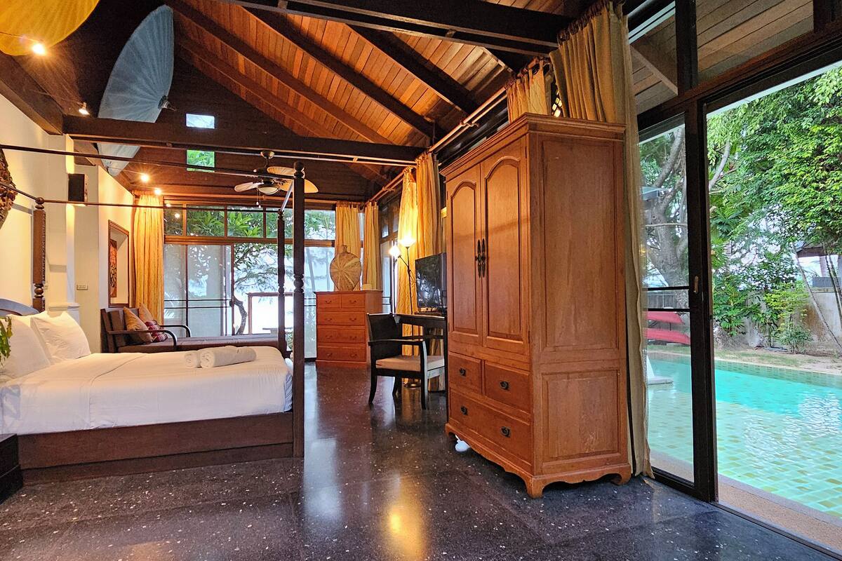 Una habitación amplia con un gran armario de madera, una cama con sábanas blancas y vistas a una piscina por medio de una puerta de cristal.