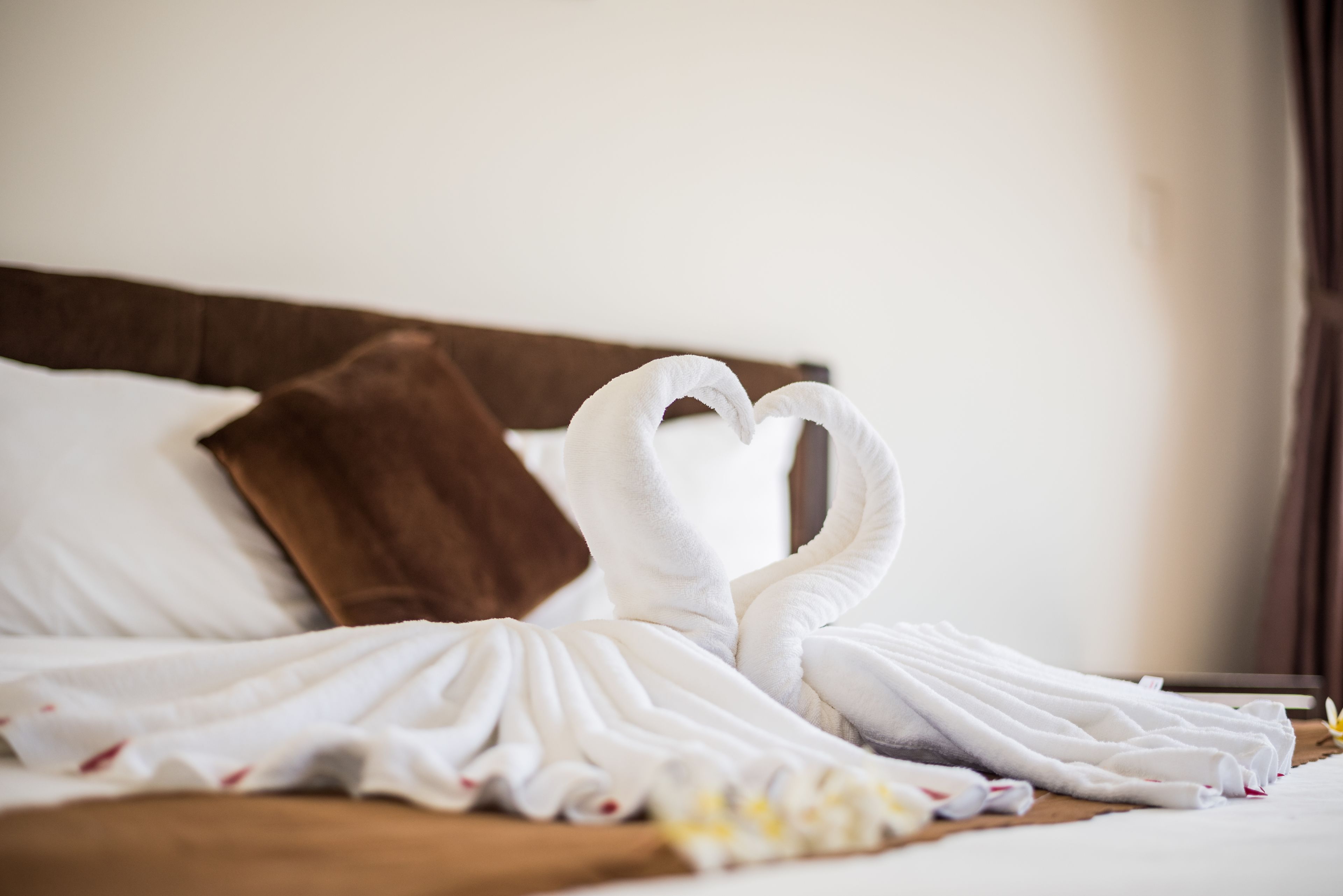 A bed with white towels arranged in a heart shape, a brown pillow, and a floral arrangement.