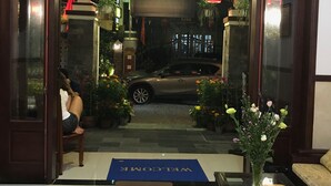 A hotel entrance with a car parked outside, a welcome mat, and a potted plant. - Miss Ten Homestay (Da Nang)