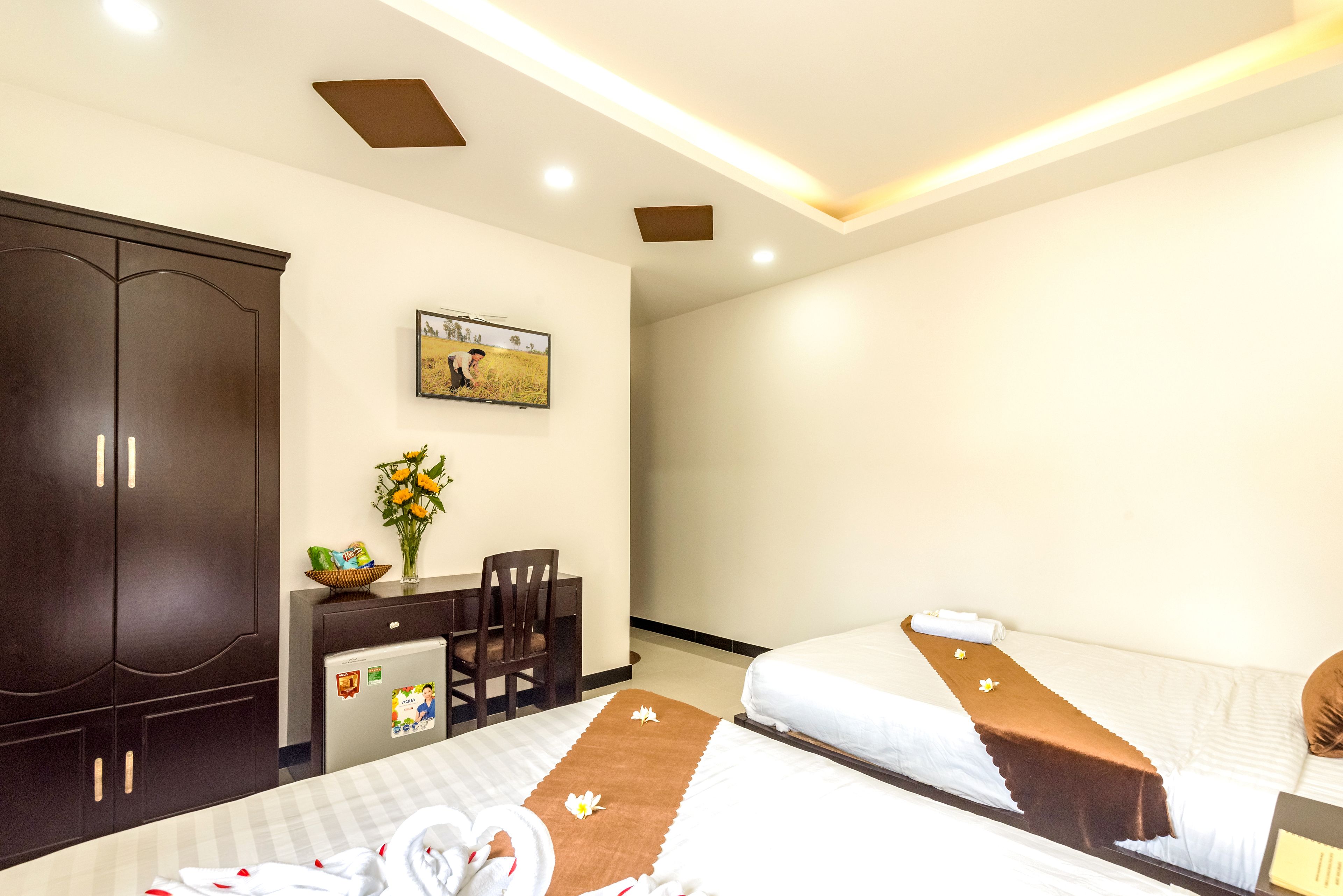 A hotel room with two beds, a desk, a chair, a wardrobe, and a painting on the wall.