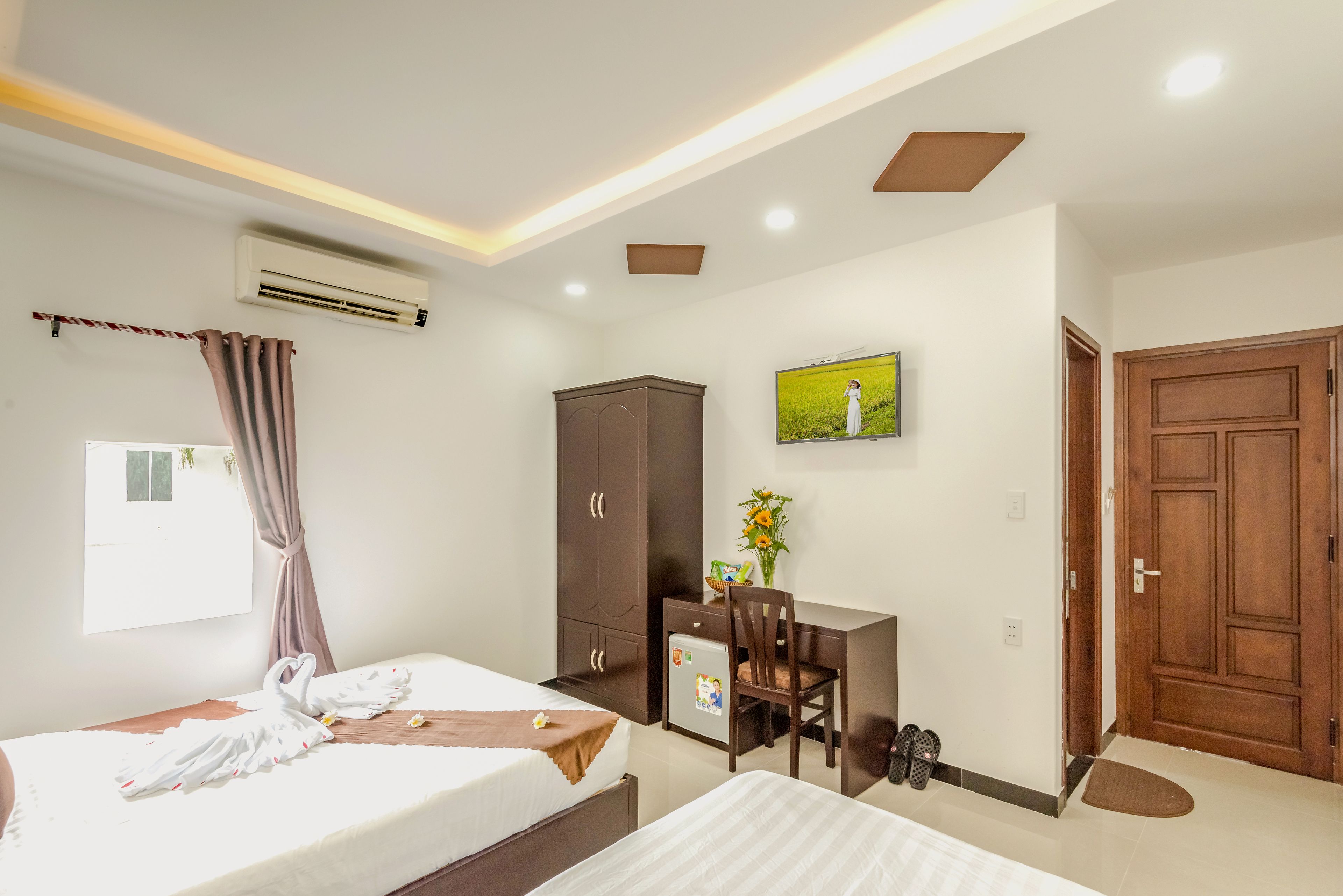 A hotel room with a bed, a desk, a chair, an air conditioner, a TV, and a wardrobe.