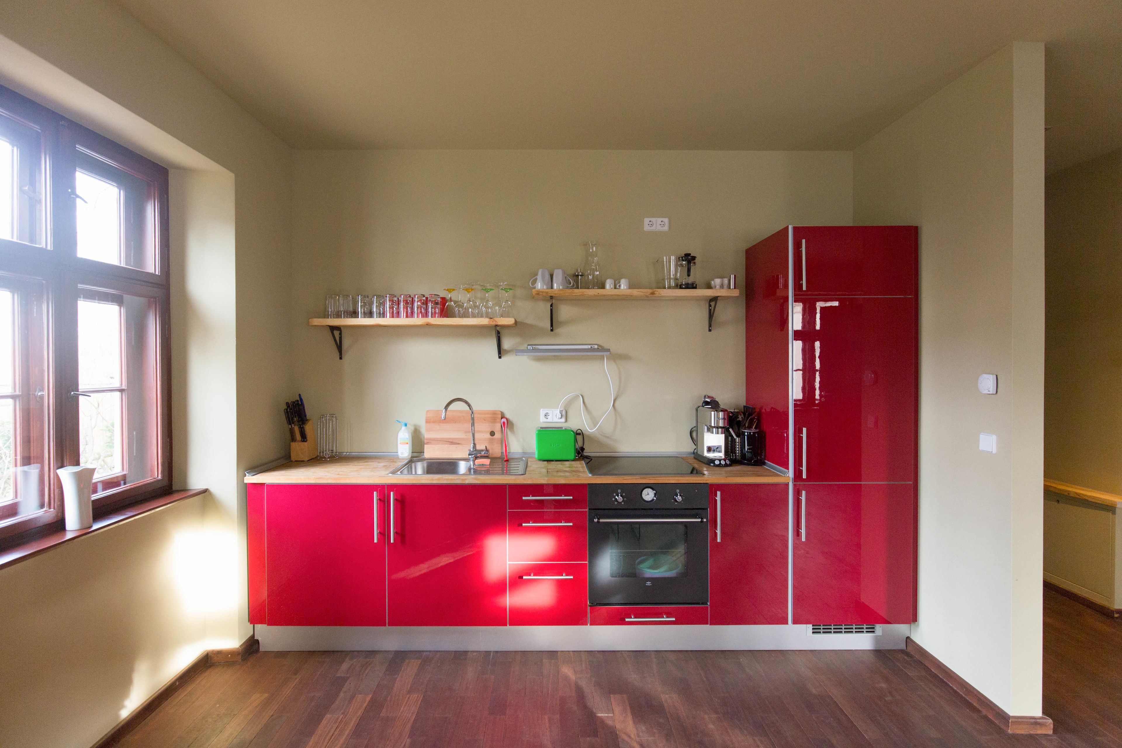 Una cocina compacta con armarios rojos, horno empotrado y ventana que proporciona luz natural.