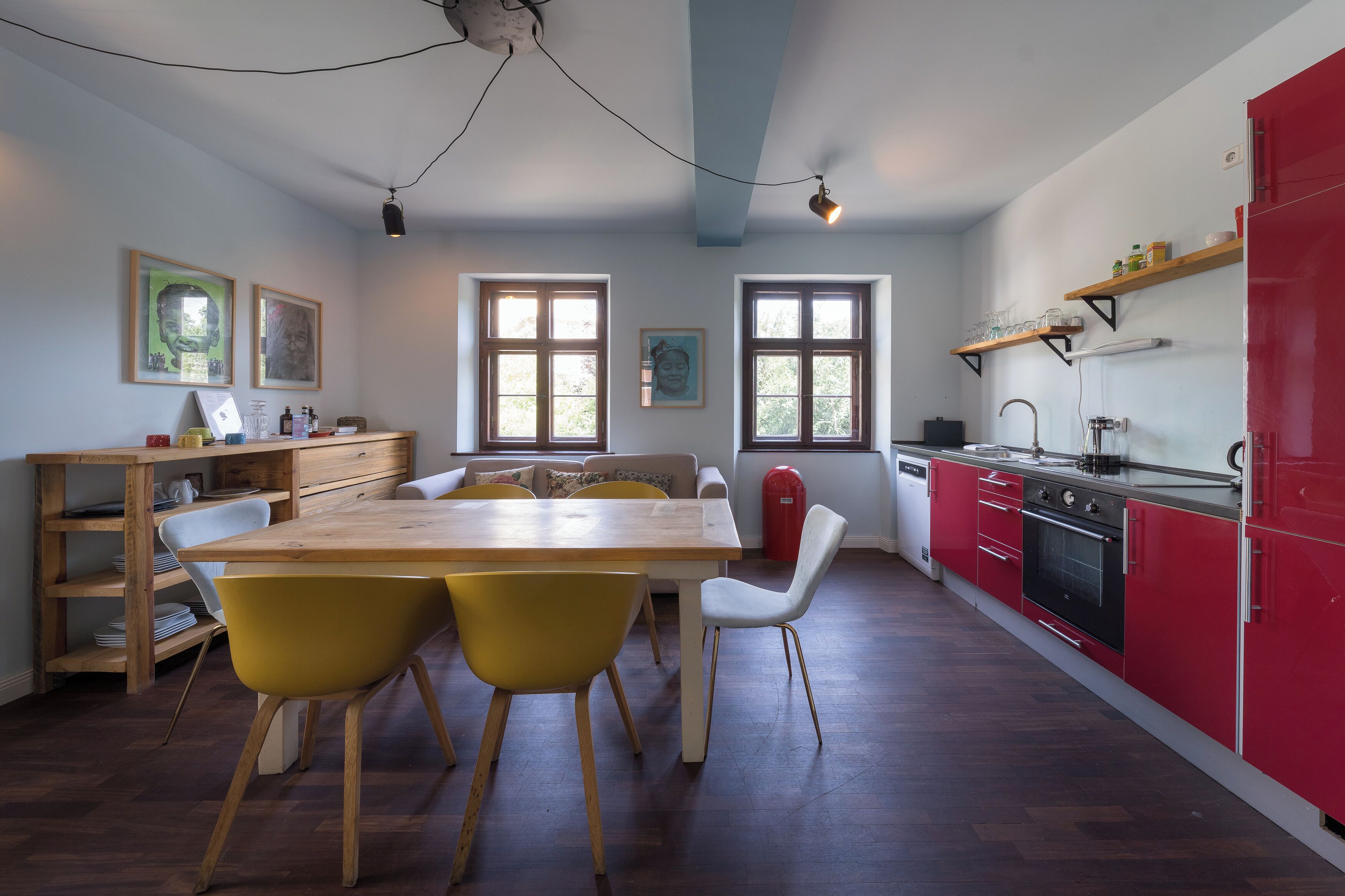 Cozinha moderna com mesa de madeira, cadeiras amarelas, geladeira vermelha e janela com vista para árvores.