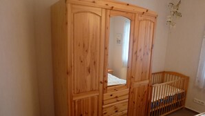 Un'armadietto in legno con uno specchio, una culla e un letto in una camera da letto.