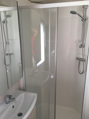 A modern bathroom with a glass shower enclosure, a sink, and a handheld showerhead. - La Sensation (Matringhem)