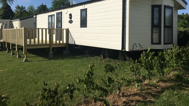 Une maison mobile de plain-pied dotée d’une terrasse, d’un petit porche et d’une fenêtre offrant une vue sur la verdure environnante.