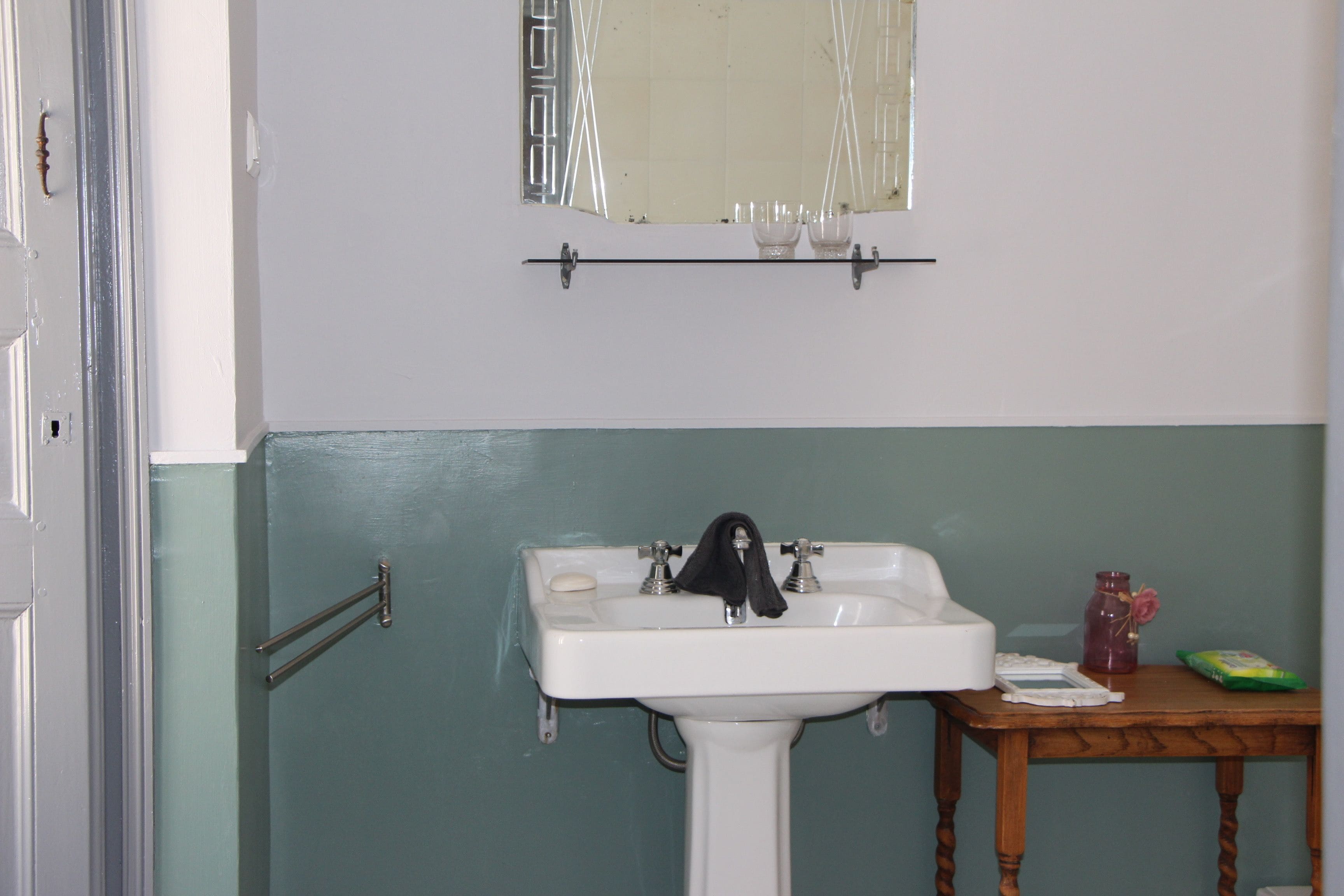 A bathroom with a white sink, a mirror above it, and a small table with toiletries.